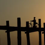 Personne avec vélo sur un pont en bois au coucher du soleil