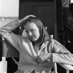 Femme en foulard et manteau assise dans une chaise pliante sur un bateau