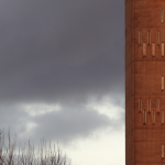 Immeuble en béton avec fenêtres étroites sous un ciel orageux.