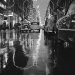 Rue animée avec décorations lumineuses et reflets sur chaussée mouillée