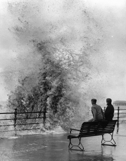 AKG1060187.webp Deux personnes sur un banc face à une forte vague – Image 1