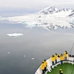 Paysage de l'Arctique avec des touristes en manteaux jaunes sur un bateau.