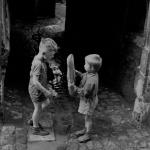 Enfants jouant avec une baguette dans une ruelle pavée