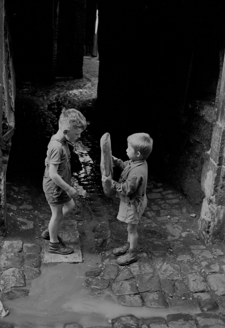 AKG1090138.webp Enfants jouant avec une baguette dans une ruelle pavée – Image 1