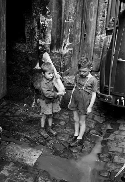 AKG1090139.webp Enfants portant du pain dans une rue pavée – Image 1