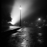 Lampadaire éclairant une rue vide par une nuit brumeuse