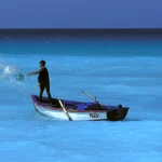 Pêcheur lançant un filet depuis un bateau en pleine mer