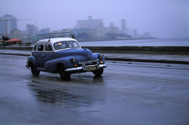 AKG1103775.webp Voiture ancienne roulant sur une route mouillée près de la mer – Image 1