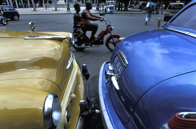 AKG1103813.webp Voitures Anciennes et Cyclomoteur Dans une Rue Animée – Image 1