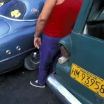Homme en débardeur rouge près de voitures classiques cubaines.