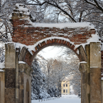 Porte en ruine sous la neige menant à une maison jaune