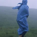 Personne en poncho bleu marchant sous la pluie dans la nature