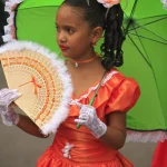 Petite Fille en Robe Rouge avec Parapluie Vert et Éventail