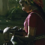 Femme en costume traditionnel jouant d'un instrument de musique dans un jardin tropical.