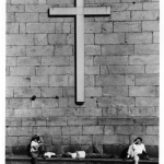 Croix sur un mur de pierre avec trois personnes se reposant à l'extérieur