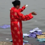 Femme en tenue traditionnelle jetant des objets dans un fleuve