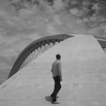 Homme marchant vers une architecture moderne sous le ciel nuageux