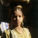 Jeune fille portant une bassine en métal sur la tête