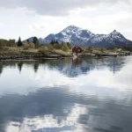 Maison rouge au bord d'un lac avec montagnes enneigées en arrière-plan