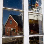 Reflet d'une maison rouge et d'un bateau dans une fenêtre sale