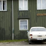 Voiture blanche garée devant une maison en bois vert.