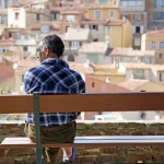 Homme assis sur un banc avec vue sur ville méditerranéenne