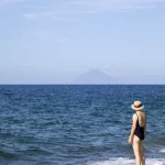 Femme sur la plage regardant la mer avec un chapeau de paille