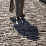 Personne marchant sur un trottoir pavé avec un sac