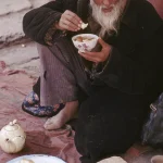 Vieil homme mangeant par terre avec une tasse à thé et une assiette