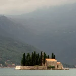 Île avec église et cyprès sur fond de montagne