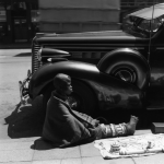 Enfant assis sur un trottoir à côté d'une voiture ancienne