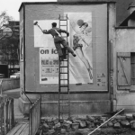 Homme collant une affiche publicitaire en noir et blanc