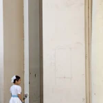Petite fille en robe blanche portant des fleurs près d'un mur