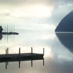Lever de soleil sur un lac paisible avec bateau et quai.