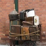 Ancienne charrette chargée de valises vintage devant un mur de briques