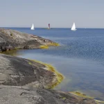 Voiliers au large d'une côte rocheuse avec phare en arrière-plan