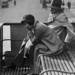 Deux personnes en trench-coat assises sur un banc en plein air