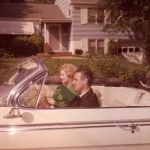 Couple dans une décapotable devant une maison suburbana