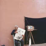 Homme âgé lisant un journal à côté d'un appareil photo ancien en extérieur