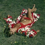 Femme en maillot de bain rouge et peignoir à fleurs allongée dans l'herbe