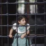 Petite fille regardant à travers une grille en fer