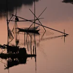 Pêcheur asiatique au crépuscule sur un lac tranquille