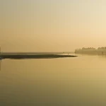 Lever du soleil sur un lac tranquille avec barque et végétation en arrière-plan