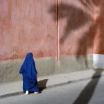 Femme en bleu marchant le long d'un mur en stuc.