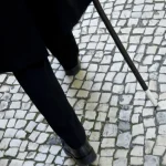 Personne âgée marchant avec une canne sur un trottoir pavé