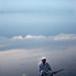 Homme en bateau sur un lac paisible avec montagnes en arrière-plan
