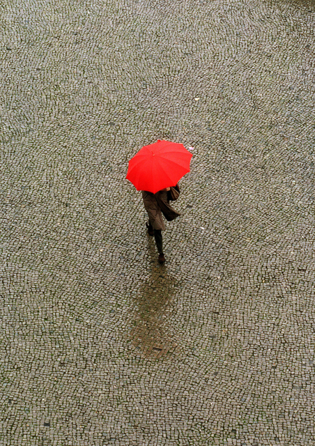AKG2725220.webp Personne avec un parapluie rouge sur une place pavée – Image 1