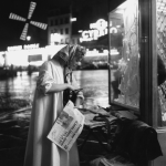 Femme achetant un journal la nuit à Paris devant le Moulin Rouge