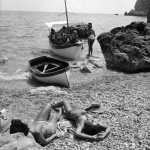 Plage de galets avec personnes prenant le soleil et bateau amarré