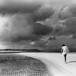 Marche solitaire sur une plage déserte sous ciel orageux